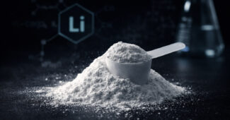 Nahaufnahme von weißem Lithium-Pulver in einem Messlöffel auf dunkler Oberfläche, im Hintergrund Laborglas und ein unscharfes ‚Li‘-Symbol.